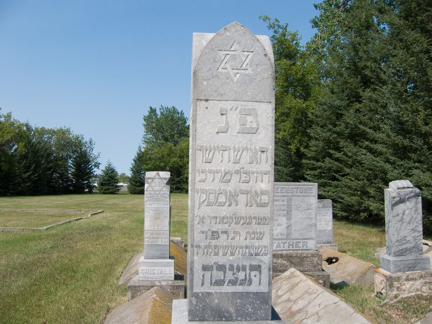 Tall white marble gravestone with a Star of David and Hebrew inscription in a prairie cemetery